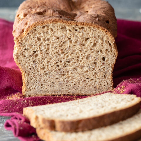 Loaf of gluten-free bread sitting on pink towel partially cut, with 3 slices sitting laying flat