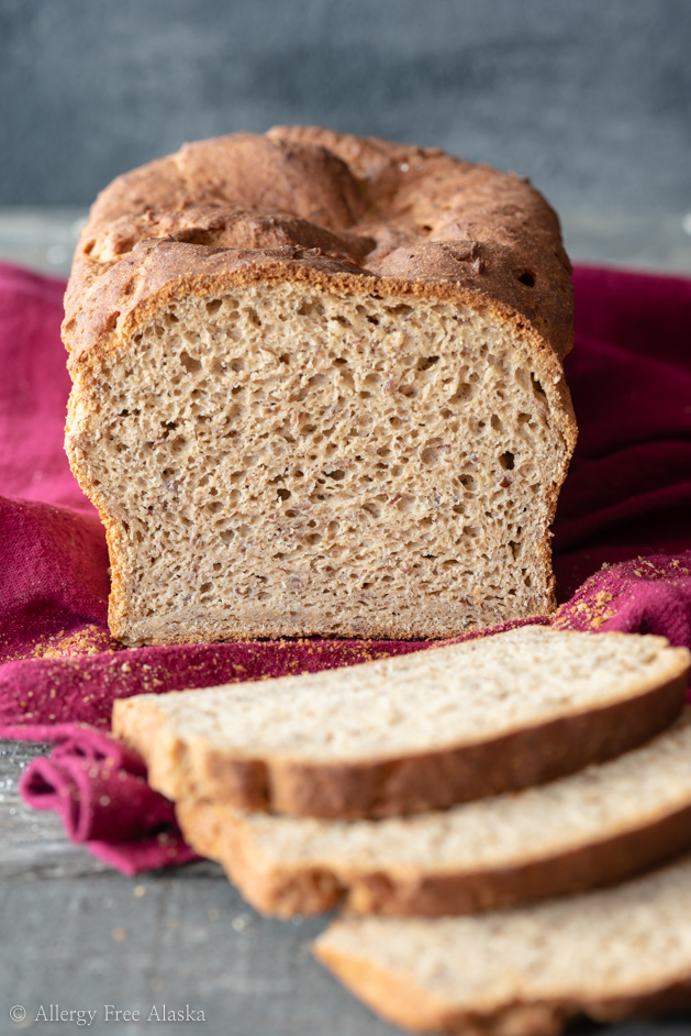 Loaf of gluten-free bread sitting on pink towel partially cut, with 3 slices sitting laying flat