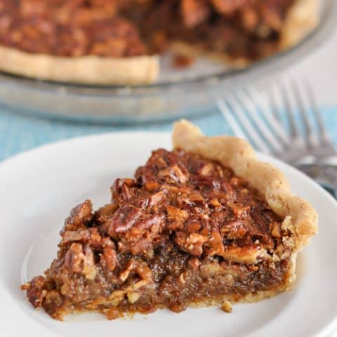 slice of gluten-free pecan pie sitting on stacked plates with cut pie in background