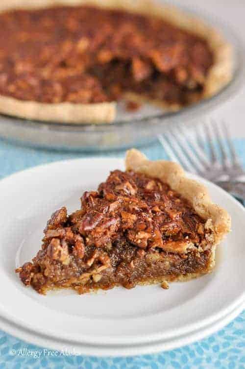 slice of gluten-free pecan pie sitting on stacked plates with cut pie in background