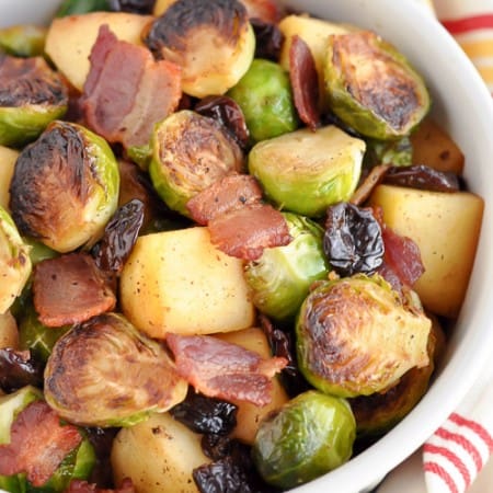 overhead shot at different angle of brussel sprouts with apples and bacon in white bowl with cream napkin with colorful stripes