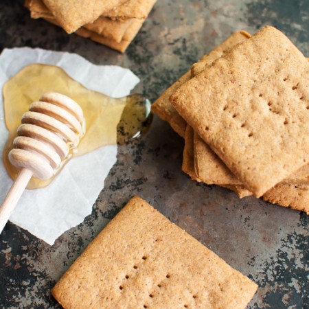 graham crackers scattered on a dark countertop aside a honey dipper dipped in honey
