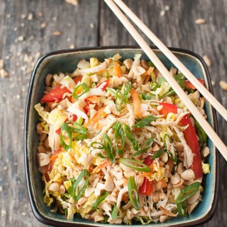 a square bowl filled with asian cabbage and chicken salad and chopsticks on the edge of the bowl