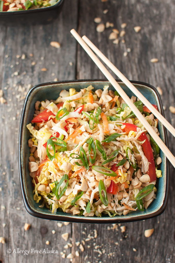 a square bowl filled with asian cabbage and chicken salad and chopsticks on the edge of the bowl