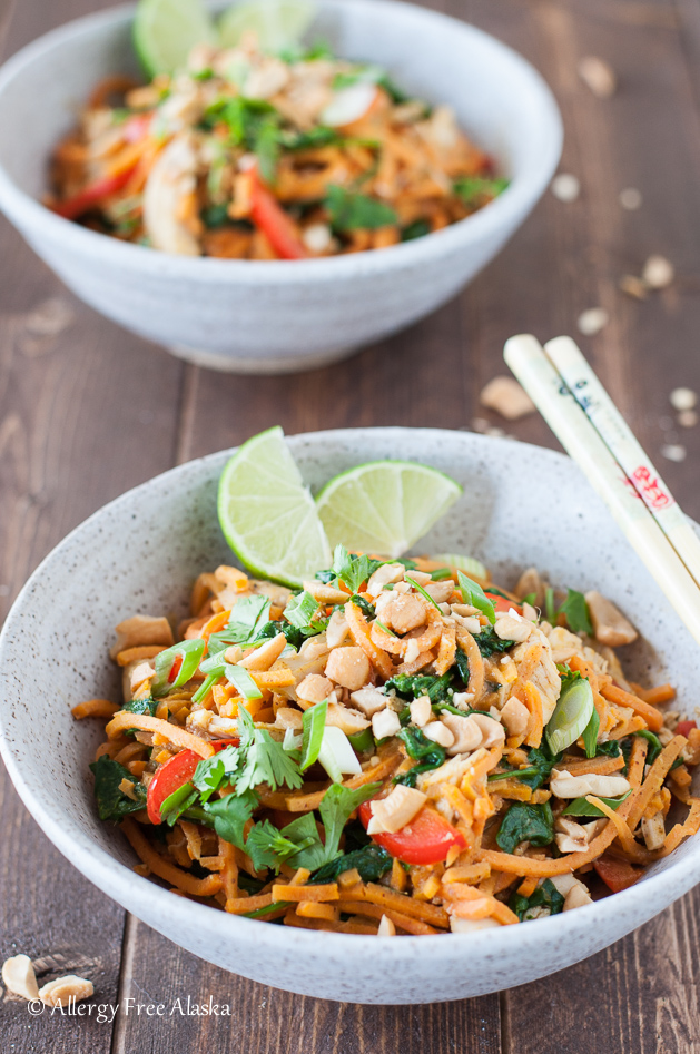 a bowl filled with sweet potato noodles, chicken, spinach, chopped cashews, and lime wedges