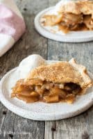 Slice of gluten-free apple pie sitting on white plate with scoop of ice cream. 2nd plate with pie in the far background.