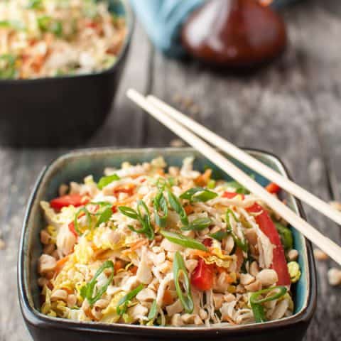 a bowl of a colorful cabbage salad with chicken and green herbs with chopsticks