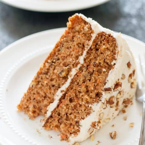 slice of gluten free carrot cake on white plate with fork, sitting on blue background