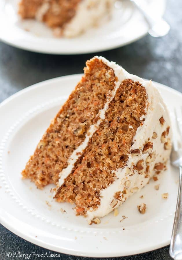 slice of gluten free carrot cake on white plate with fork, sitting on blue background