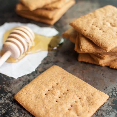 graham crackers scattered on a dark countertop aside a honey dipper dipped in honey