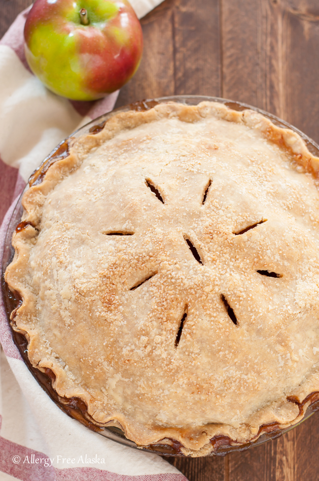 baked whole vegan apple pie, on dark brown background, with cream and red kitchen towel and apple