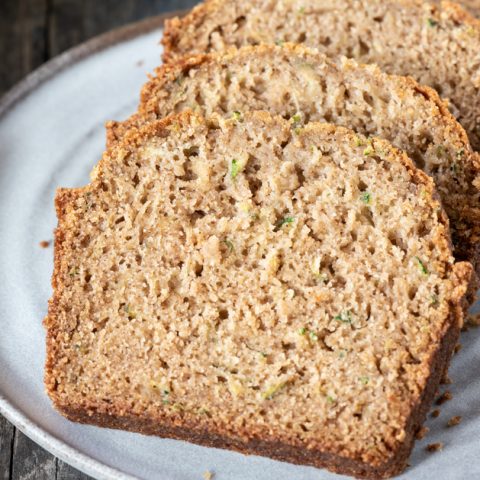 at different angle: sliced gluten free zucchini bread on gray plate with blue napkin in background