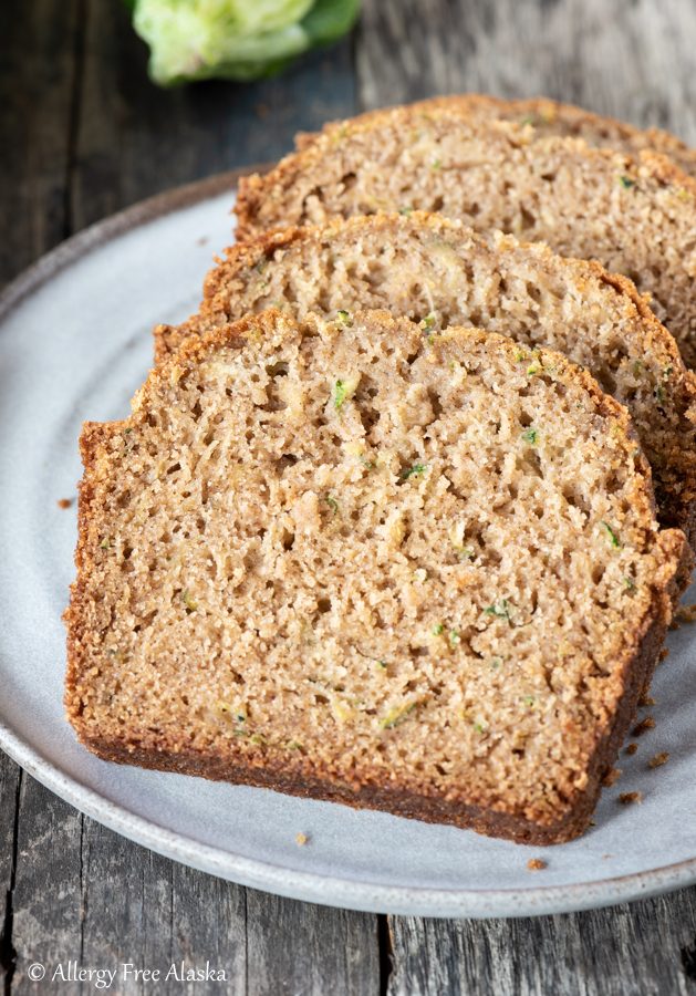 at different angle: sliced gluten free zucchini bread on gray plate with blue napkin in background