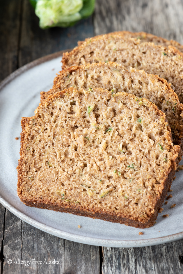 at different angle: sliced gluten free zucchini bread on gray plate with blue napkin in background