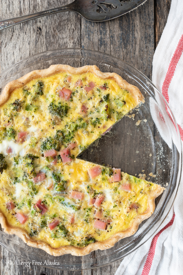 overhead shot of dairy-free quiche in clear pie plate with a slice missing