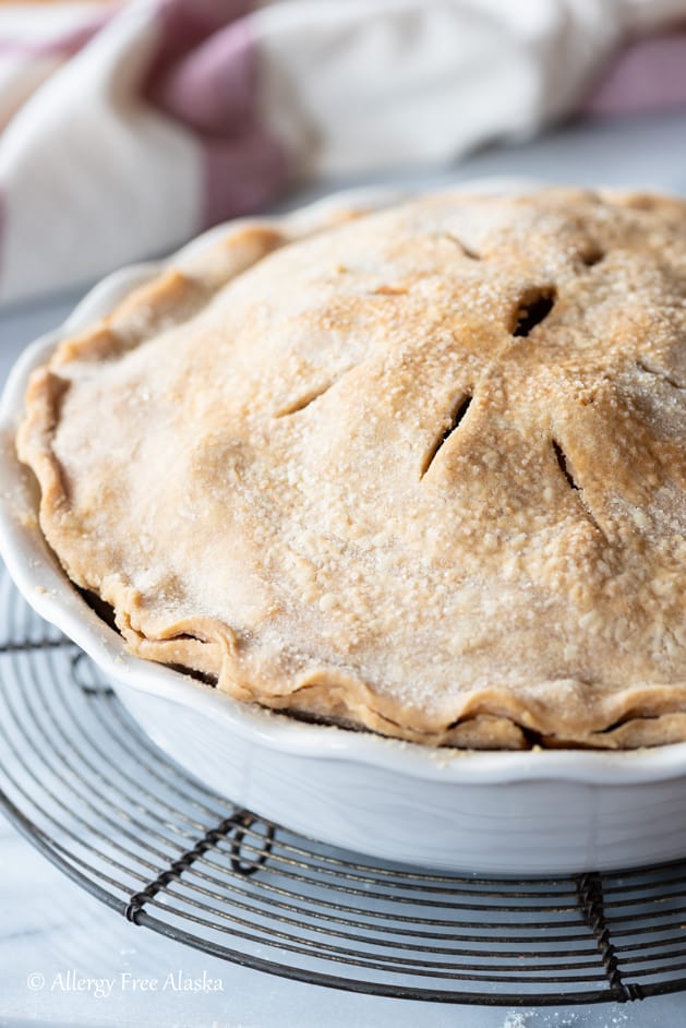 baked whole apple pie sitting on black cooling rack with white and red napkin in background