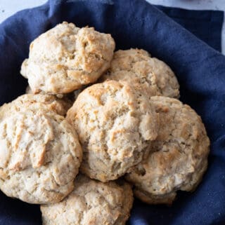 gluten-free biscuits sitting in blue napkin lined basket, with small bowl of jam off to side