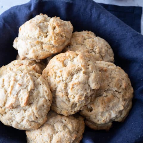 gluten-free biscuits sitting in blue napkin lined basket, with small bowl of jam off to side