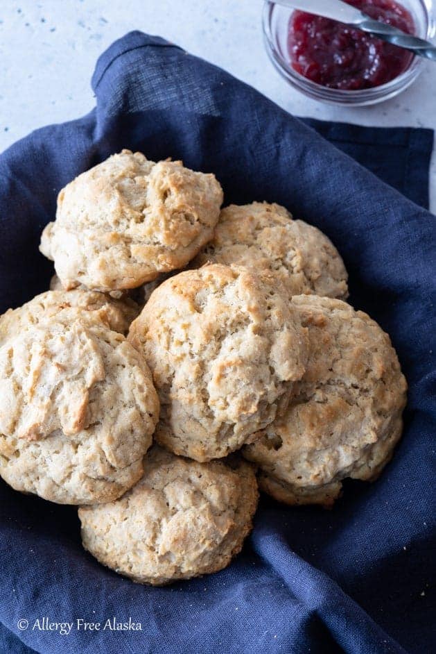 gluten-free biscuits sitting in blue napkin lined basket, with small bowl of jam off to side