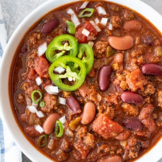 Top down view of a chili in white bowl sitting on blue background