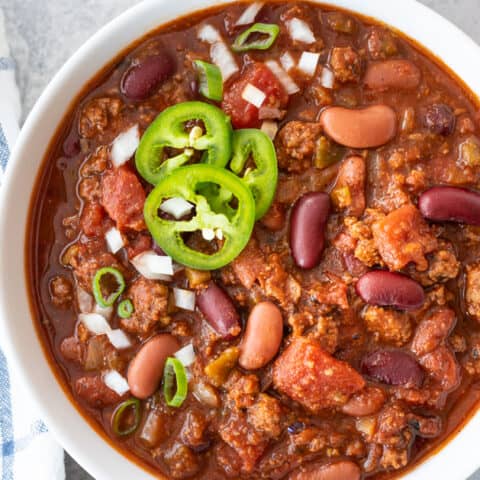 Top down view of a chili in white bowl sitting on blue background