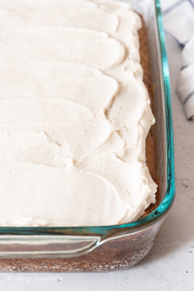 frosted gluten-free banana cake in glass pan sitting on light gray background