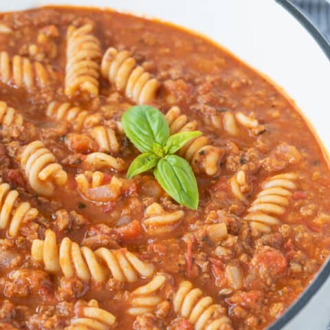 gluten-free lasagna soup sitting in white dutch oven with sprig of basil in it