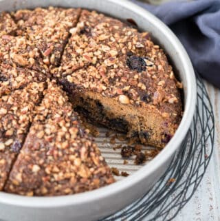 Side angle shot of sliced gluten free coffee cake in metal pan sitting on wire rack