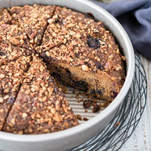 Side angle shot of sliced gluten free coffee cake in metal pan sitting on wire rack