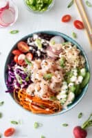 Top down view of shrimp poke bowl on white background sprinkled with green onion and cherry tomato halves