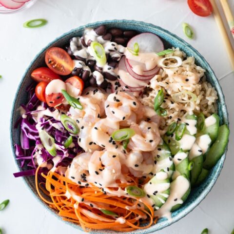 Top down view of shrimp poke bowl on white background sprinkled with green onion and cherry tomato halves