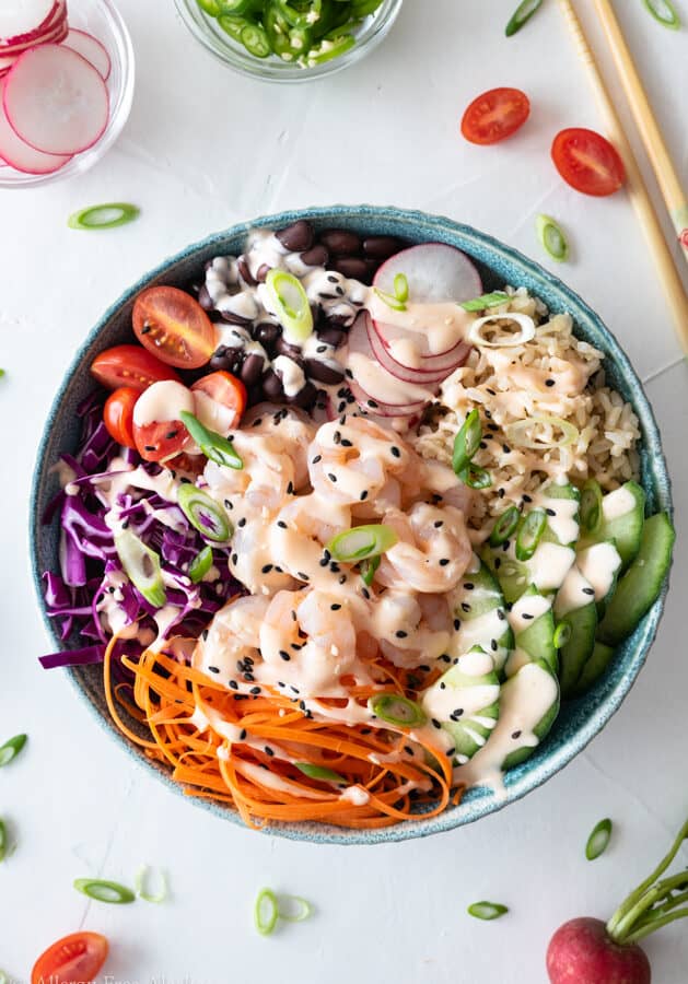 Top down view of shrimp poke bowl on white background sprinkled with green onion and cherry tomato halves