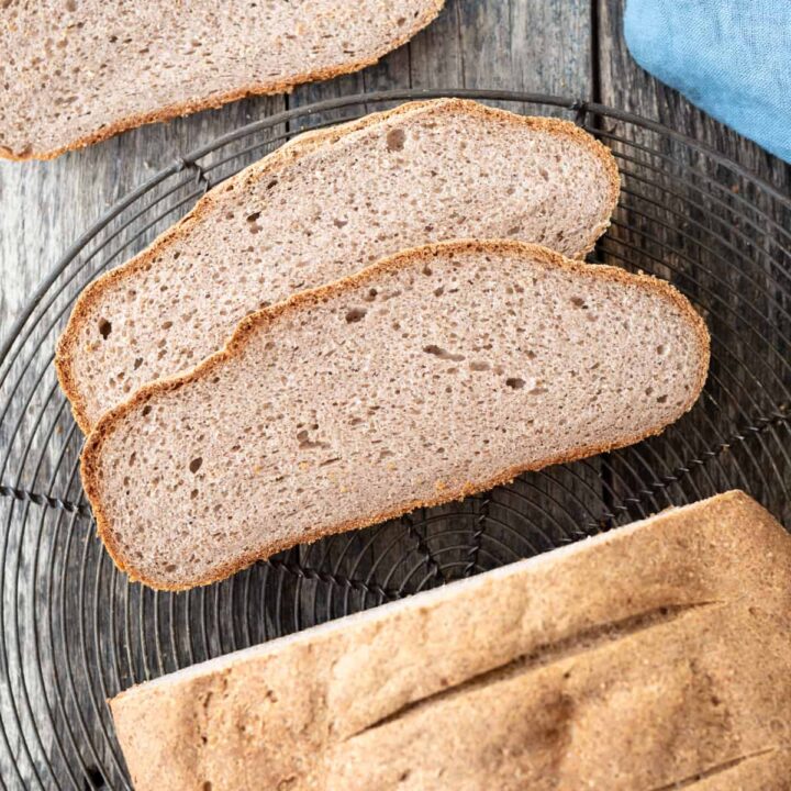 top down view of half sliced buckwheat bread sitting on wire cooling rack on gray/blue background