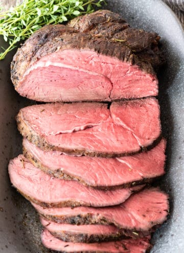 top down view of partially sliced sirloin tip roast sitting on gray platter with handful of fresh thyme