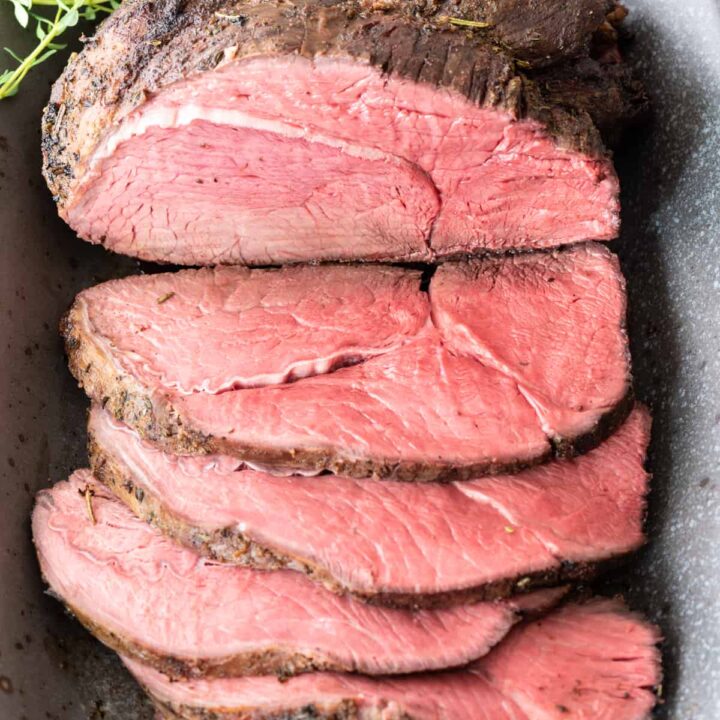 top down view of partially sliced sirloin tip roast sitting on gray platter with handful of fresh thyme