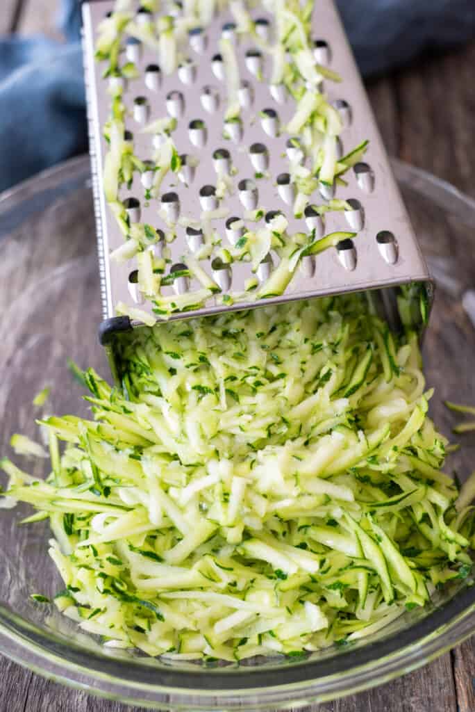kitchen grater sitting in clear pie plate with grated zucchini