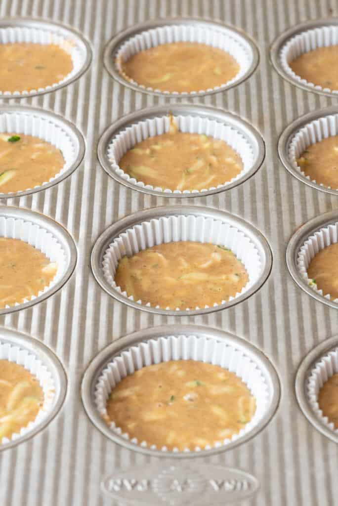gluten free zucchini batter in muffin tins lined with white paper liners