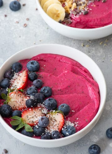 at different angle: vibrant pink dragon fruit smoothie in a white bowl, topped with blueberries, strawberries, and flaked coconut