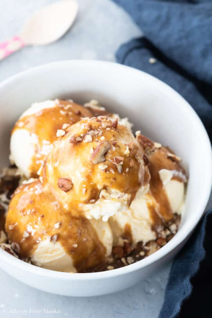 vanilla ice cream covered in vegan caramel sauce and chopped pecans, in white bowl on blue background