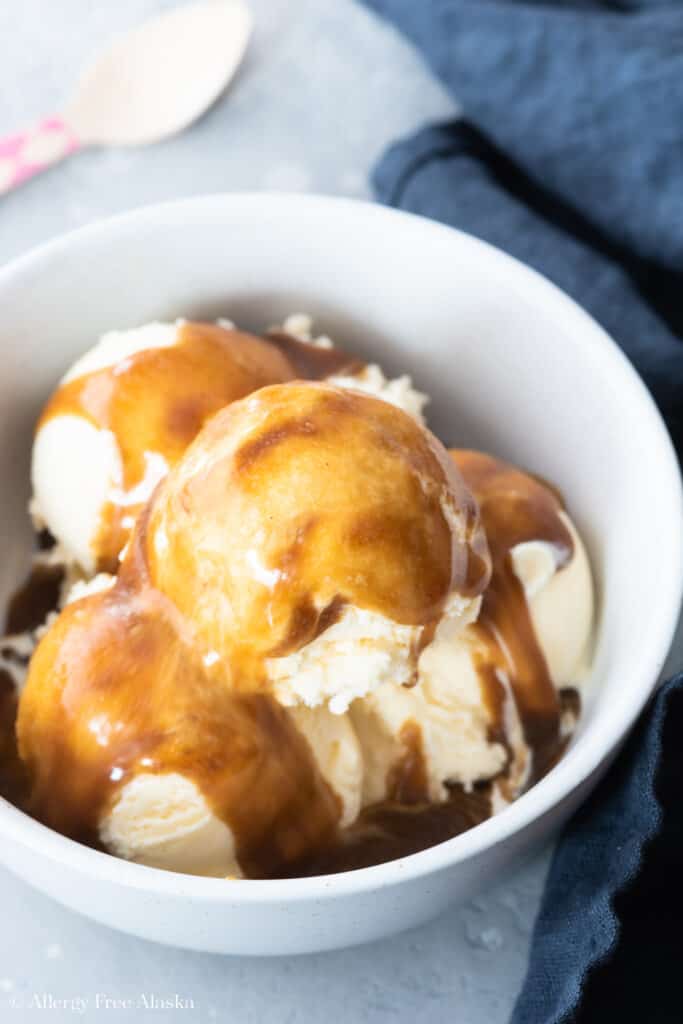 vanilla ice cream covered in vegan caramel sauce, in white bowl on blue background