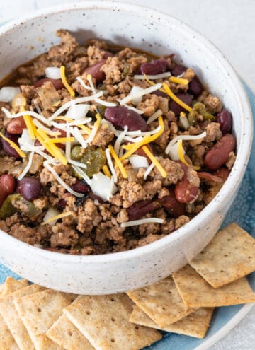 top down view of white/brown speckled bowl of chili without tomotoes sitting on blue plate with crackers
