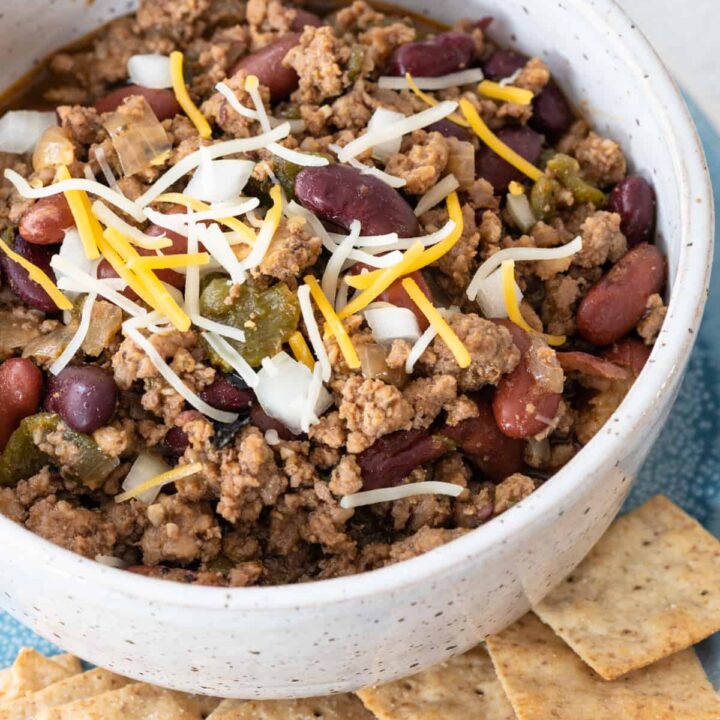 top down view of white/brown speckled bowl of chili without tomotoes sitting on blue plate with crackers