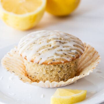 gluten free lemon poppy seed muffin sitting on paper muffin liner on white plate with slice of lemon