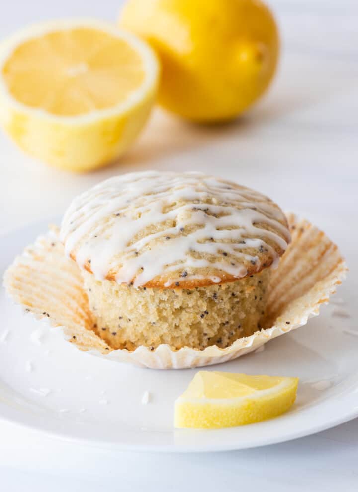 gluten free lemon poppy seed muffin sitting on paper muffin liner on white plate with slice of lemon