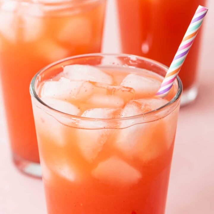 at different angle: 3 strawberry acai refreshers in clear glasses with multicolored staws, sitting on pink background