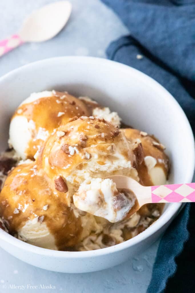 vanilla ice cream covered in vegan caramel sauce and chopped pecans, in white bowl on blue background