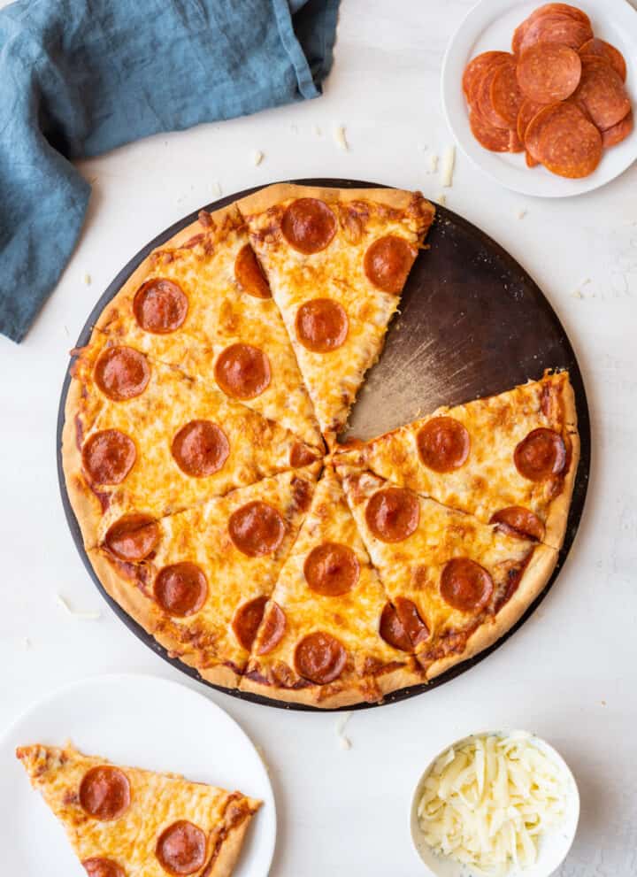 Top down view pepperoni pizza gluten free with missing slice to side on white plate