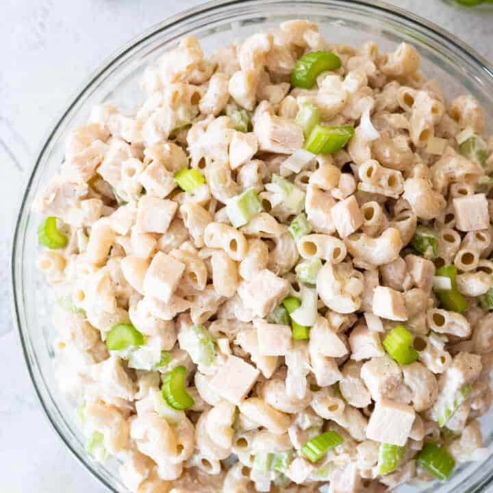 Top down view at different angle of gluten free macaroni salad in clear bowl on gray background. clear bowls of other ingredients in background