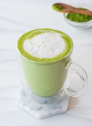 coconut matcha latte in clear mug sitting on marble coaster on gray background
