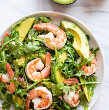 close up view of prawn and avocado salad on white plate, with halved avocado in background